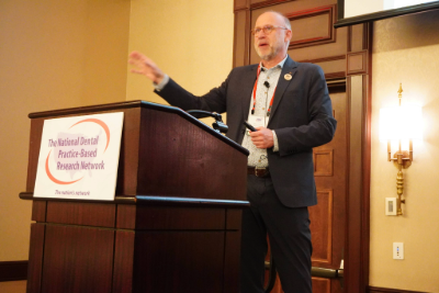 Image of man in suit talking at a podium with a sign that says
